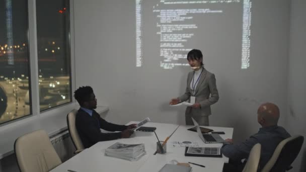 成功した若いアジアの女性ソフトウェアエンジニアの高角度は 正式なスーツを着て 白い壁のそばに立ってコンピュータコードの投影 プレゼンテーション 同僚の質問をする — ストック動画