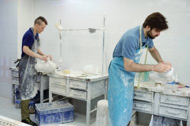 Protez fabrikasında çalışan iki genç erkek işçi masaların başında bekliyor.