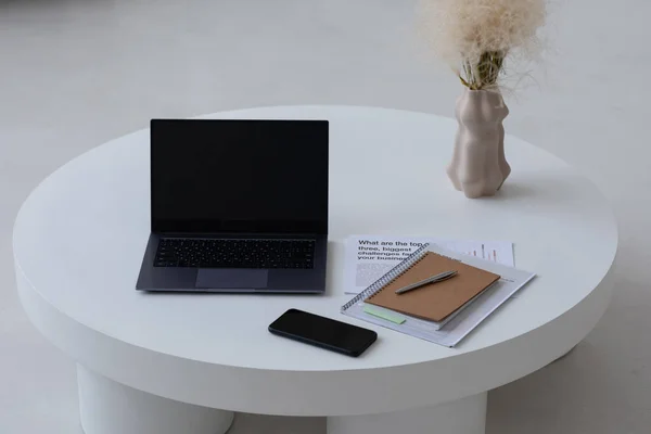 Kleine minimale ronde tafel met laptop, mobiele telefoon, notebook, papieren en vaas — Stockfoto