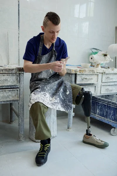 Jonge rustgevende man met een handicap zit door kleine tafel in prothetische werkplaats — Stockfoto