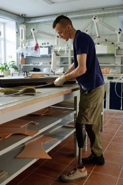 Jongeman met een handicap staat klaar bij de werkplek tijdens het snijden van opgerold materiaal — Stockfoto