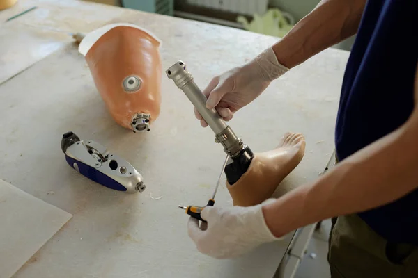 Ręce rękawiczki pracownika fizycznego trzymającego śrubokręt i część protezy nogi — Zdjęcie stockowe