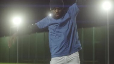 Orta uzunluktaki Afro-Amerikan erkek sporcu üniforması giyiyor, geceleri spot ışıklarıyla futbol sahasında geriniyor.