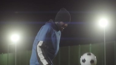 Formalı ve kalın şapkalı Afro-Amerikan erkek sporcunun orta boy portresi, topla futbol hareketleri çalışması, sonra gece spot ışıklarıyla futbol sahasında poz vermesi.