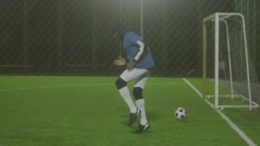 Formalı ve kalın şapkalı Afro-Amerikan erkek sporcunun tam bir yan görüntüsü, ısınma noktası. Sonra gece spot ışıklarıyla futbol sahasına gidiyor.
