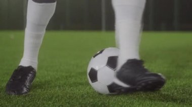 Çerçevede bacakları olan düşük açılı bir sporcu sadece yeşil çimlerin üzerinde futbol topu etrafında numaralar yapıyor.