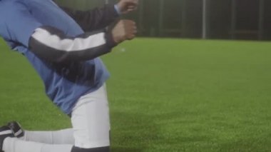 Spor kıyafetleri ve kalın şapkalar giyen, futbol sahasında çimlere düşen, golü kutlayan, ünlü bir oyuncu olmayı hayal eden genç siyahi bir adam.