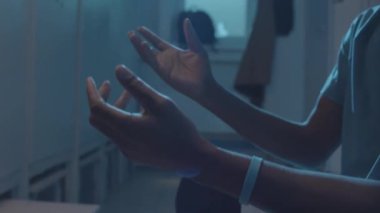 Kırpılmış erkek sporcunun orta bölümü soyunma odasında oturmuş futbol topu fırlatıyor.