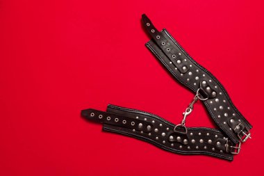 Siyah deri askılı kırmızı pankart ve kelepçeli eller ve bacaklar için metal perçinler ve seks oyunları. BDSM deneği. Yetişkin ürünleri ve seks oyuncakları mağazası reklamı için arka plan.