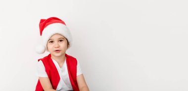 Beyaz arka planda izole edilmiş kırmızı Noel Baba şapkalı ve kostümlü güzel mutlu çocuk portresi. Beş yaşında Avrupalı bir çocuk. Pankart. Uzayı kopyala Noel zamanı model tasarımı. Yeni yıl tatili.