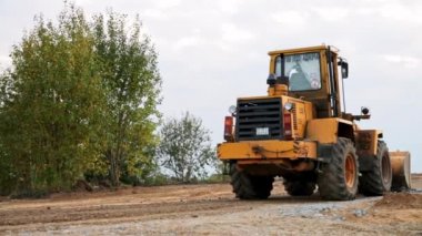 Belarus, Minsk - 8 Ekim 2021: çekici buldozer yakın çekim yapar. Önden doldurucu kova kullanıyor. Yol yapımı. Büyük kazıcı molozları sıkıştırıyor. Garaj yolu düzleştiriliyor. İnşaat alanı.