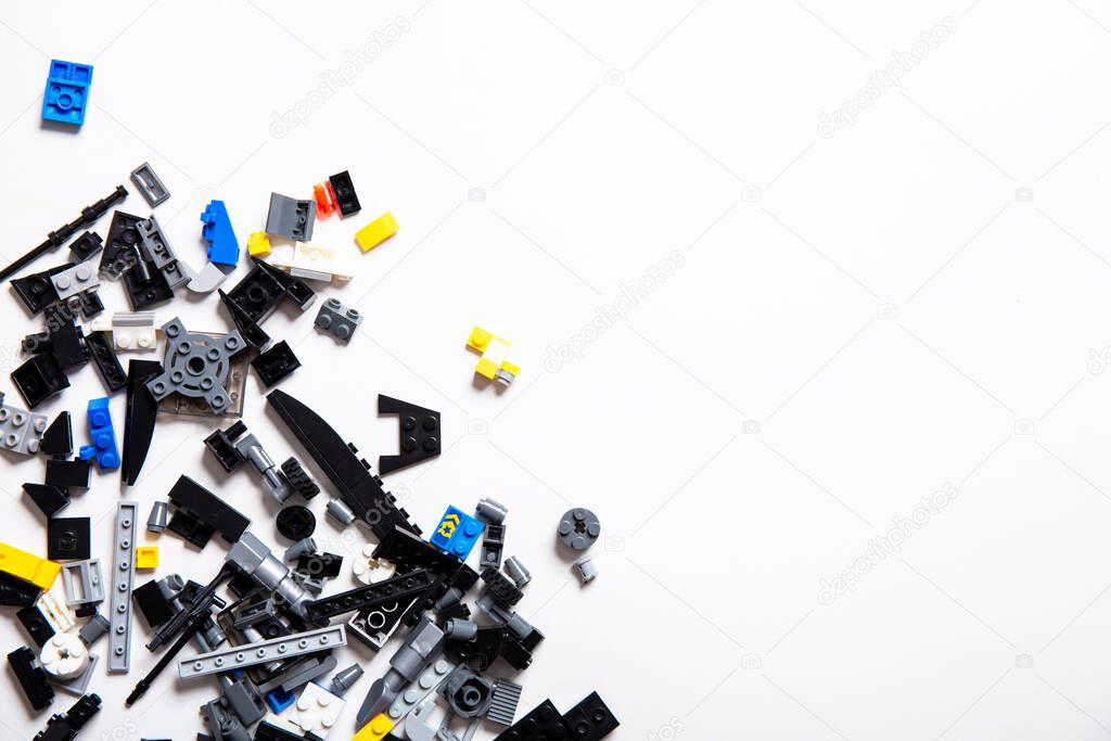 Many colored parts of children play set on a white background with copy space. Empty place for text. Gray, black, blue and yellow deals for building creative ideas. Scattered little toys. Studio shot.