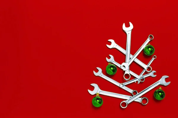 圣诞树是用红色背景的绿色球装饰的扳手做成的 有工具的新年横幅 明信片上有问候语的地方 新年快乐 工业假日的概念 复制空间 图库照片