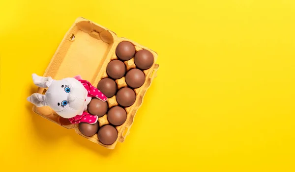 Balení deseti čokoládových vajec s načechraným bílým králíčkem na žlutém pozadí s kopírovacím prostorem, prázdné textové místo. Banner pro náboženské svátky. Návrhářství. Zábavné Velikonoční lovecké přání. Ručně vyráběný dekor — Stock fotografie