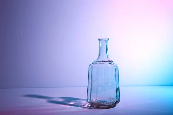 Glass bottle with copy space. Large creative vintage vase. Graphic still life with light and shadow in multicolor neon light. An art object. Recyclable material. The concept of alcoholism. Open flask Royalty Free Stock Photos