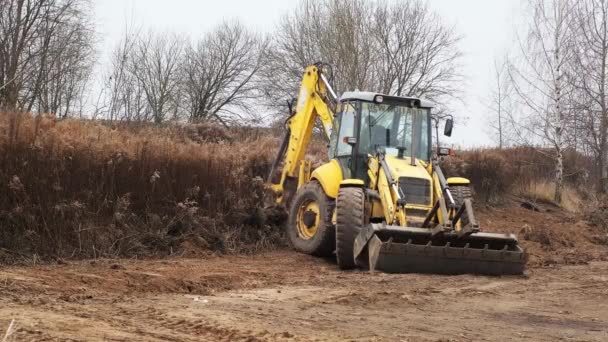 Campo de niveles de tractor. Retroexcavadora limpiando el sitio de construcción. Bulldozer prepara el terreno de construcción. Equipo de transporte terrestre. Un graduado. Cubo cargador frontal. Belarús, Minsk 17 de noviembre de 2021 — Vídeo de stock