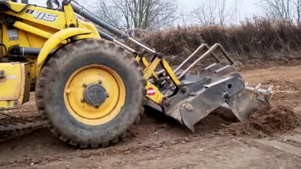 Hladinové pole traktoru. Backhoe nakladač čistí staveniště. Buldozer připravuje staveniště. Přepravní zařízení pozemšťanů. Grader. Kbelík předního nakladače. Bělorusko, Minsk 17. listopadu 2021 — Stock video