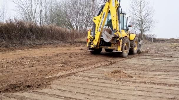 Campo de niveles de tractor. Retroexcavadora limpiando el sitio de construcción. Bulldozer prepara el terreno de construcción. Equipo de transporte terrestre. Un graduado. Cubo cargador frontal. Belarús, Minsk 17 de noviembre de 2021 — Vídeo de stock