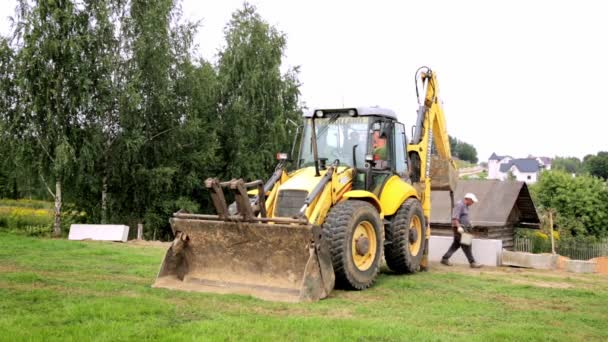 Hjullastare. Grävmaskinen monterar grundstenarna i ett dike. Behåller väggbyggnaden. Byggarbetsplats. Arbetarna sköter installationen. Full HD-video. Semkovo, Vitryssland - 3 september 2021 — Stockvideo