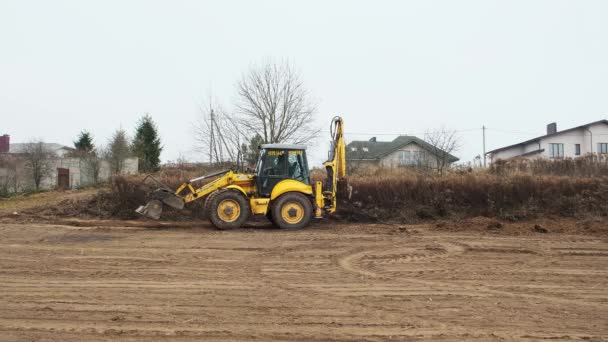 Hladinové pole traktoru. Backhoe nakladač čistí staveniště. Buldozer připravuje staveniště. Přepravní zařízení pozemšťanů. Grader. Kbelík předního nakladače. Bělorusko, Minsk 17. listopadu 2021 — Stock video