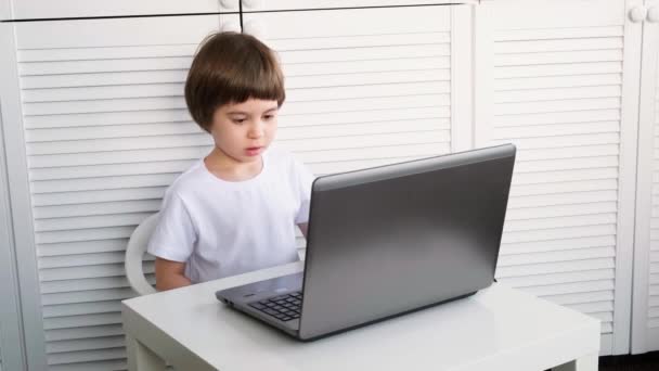 5 살짜리 남자 아이가 테이블에 앉아서 노트북으로 화면을 보고 있습니다. 아이들은 숙제를 하고, 비디오 게임을 하고 , IT 개발을 공부하고, 만화를 보고 있습니다. 홈 스트리트 온라인 교육 개념 — 비디오