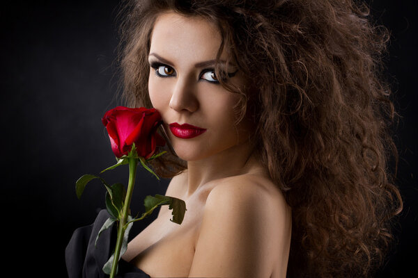 Closeup portrait of a glamorous young womanl with red rose on dark background