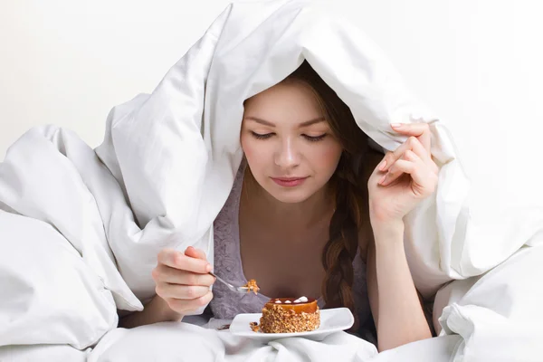 Girl eating cake under cover — Stock Photo, Image