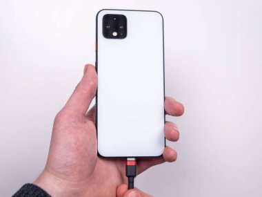 Smartphone is connected to the charger on a white background top view. Discharged battery. Low battery. Smartphone plug in on a charger.