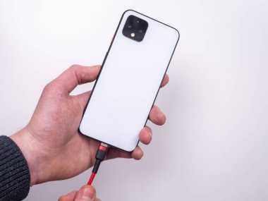 Akıllı telefon, beyaz arka plandaki şarj cihazına bağlıdır. Şarjı bitti. Şarjım bitiyor. Akıllı telefon şarj aletinin fişini tak.