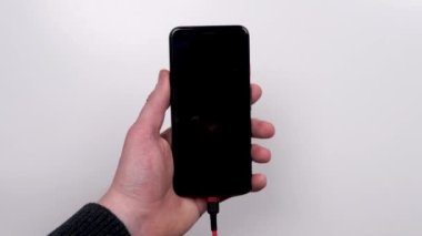 Smartphone is connected to the charger on a white background top view. Discharged battery. Low battery. Smartphone plug in on a charger.