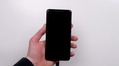 Smartphone is connected to the charger on a white background top view. Discharged battery. Low battery. Smartphone plug in on a charger.