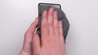 Erkek eller, beyaz arka plan görüntüsünde mikrofiber peçeteyle akıllı telefonu kirden, mikroplardan ve virüslerden siler. Akıllı telefonunu pislikten ve parmak izlerinden temizle..