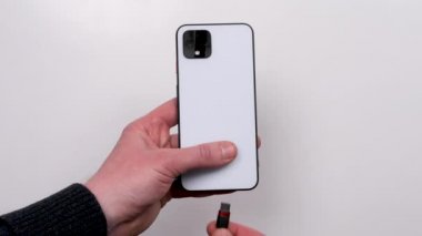 Smartphone is connected to the charger on a white background top view. Discharged battery. Low battery. Smartphone plug in on a charger.