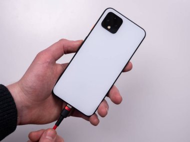 Smartphone is connected to the charger on a white background top view. Discharged battery. Low battery. Smartphone plug in on a charger.
