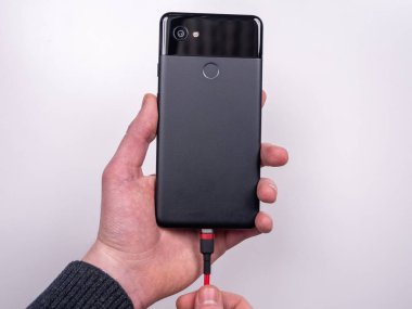 Akıllı telefon, beyaz arka plandaki şarj cihazına bağlıdır. Şarjı bitti. Şarjım bitiyor. Akıllı telefon şarj aletinin fişini tak.