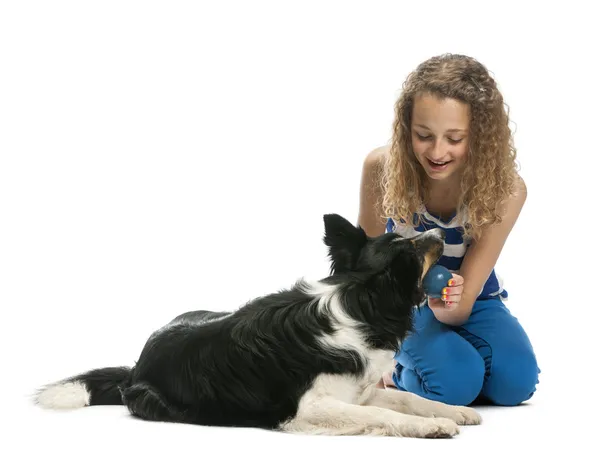 Giovane ragazza seduta e dando una palla a un confine Collie contro sfondo bianco — Foto Stock