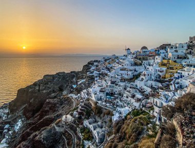 Günbatımında Ege 'deki Santorini adasındaki geleneksel beyaz mimari ve yel değirmenleriyle Oia köyünün panoramik manzarası, seyahat geçmişi, Santorini, Thera, Yunanistan