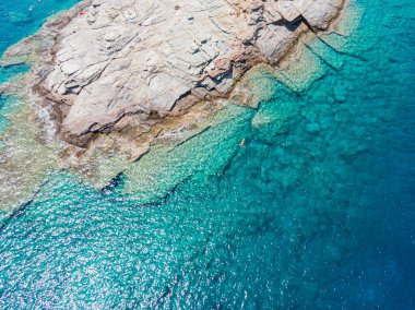 Gök mavisi su dokusunda yüzen tanınmayan bir kadın, kayalık zemini olan şeffaf bir deniz yüzeyi. Hava görüntüsü, doğal mavi arkaplan