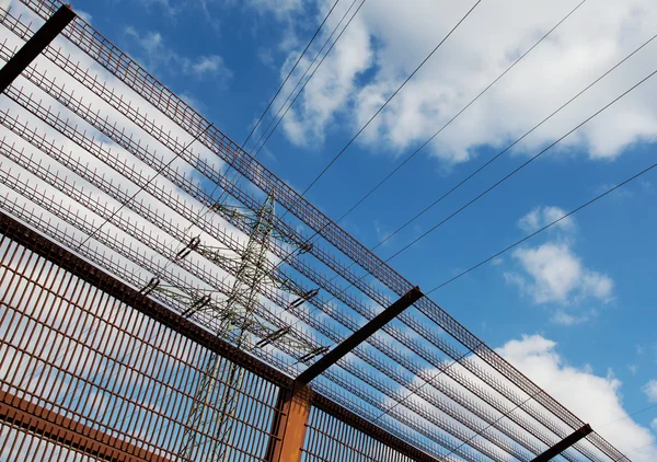 Eletricidade pilão e cerca de barreira contra o céu azul — Fotografia de Stock