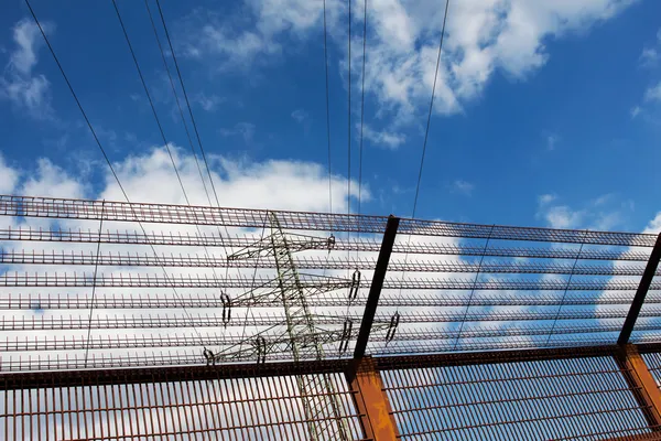 Eletricidade pilão e cerca de barreira contra o céu azul — Fotografia de Stock
