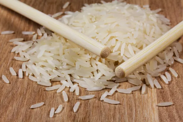 Grains de riz sur surface en bois et baguettes — Photo
