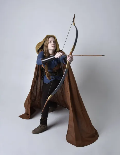 红头发女人的肖像 穿着中世纪维京风格的服装和飘逸的斗篷 手持弓箭武器 在工作室的背景下摆姿势 — 图库照片