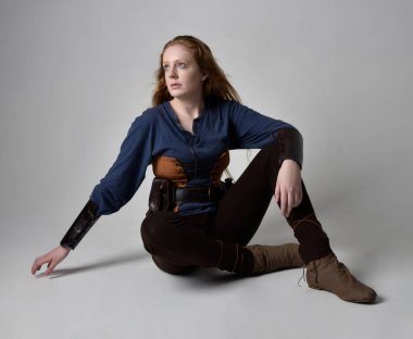 Orta çağ Viking ilham verici bir kostüm giyen, uzun bir kılıç taşıyan, stüdyo arka planında poz veren kızıl saçlı bir kadının tam boy portresi..