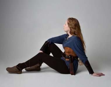 Orta çağ Viking ilham verici bir kostüm giyen, uzun bir kılıç taşıyan, stüdyo arka planında poz veren kızıl saçlı bir kadının tam boy portresi..