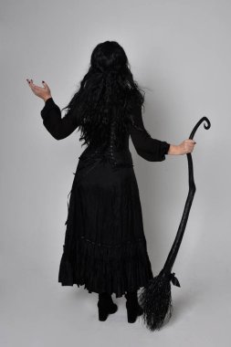 Siyah Victoria cadısı kostümü giymiş koyu renk saçlı bir kadının tam boy portresi. Ayakta duruş, arka plan, hareketli el hareketleri, stüdyo arka planı.