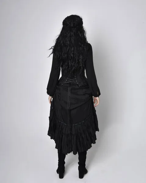 黒の勝利者の魔女の衣装を着た暗い髪の女性の完全な長さの肖像画 立ちポーズバックビュースタジオの背景に手の動きがあり — ストック写真
