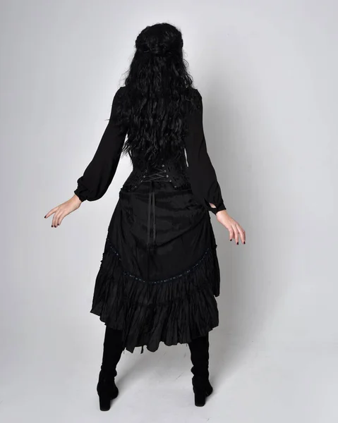 身穿黑色维多利亚式女巫服装的黑头发女人的全长肖像 倒立姿势 后视镜 有手势式的手部动作 在工作室的背景下 — 图库照片