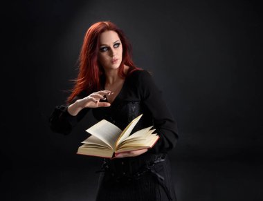 Siyah Victoria Cadı kostümü giyen kızıl saçlı kadının yakın plan portresi. Duruş, hareketli el hareketleri, karanlık stüdyo arka planı.