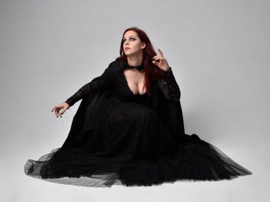 Siyah Victoria tarzı cadı kostümü giyen, stüdyo arka planında hareketli, hareketli, siyah saçlı bir kadının tam boy portresi..