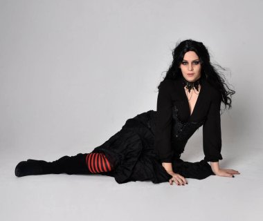 Siyah Victoria tarzı cadı kostümü giyen, stüdyo arka planında hareketli, hareketli, siyah saçlı bir kadının tam boy portresi..